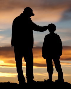 Silhouette of a father and son at sunset, with the father placing a hand on his son's head in a gesture of guidance and support, symbolizing mentorship, fatherhood, and strength.