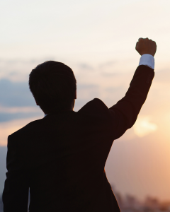 Silhouetted businessman raising his fist in victory against a sunset, symbolizing success, purpose, and achievement.