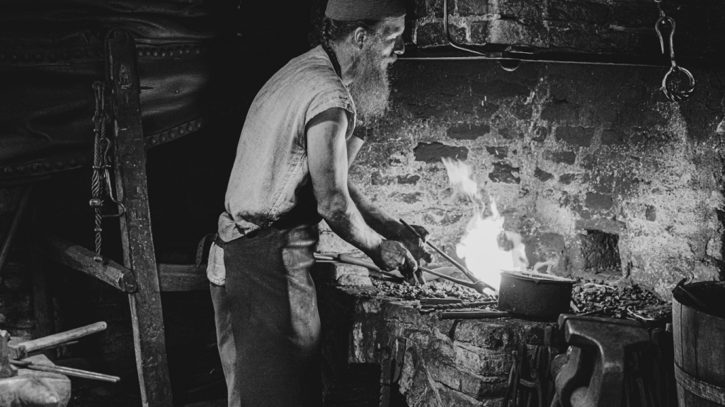 Blacksmith working at forge with hammer and tongs.