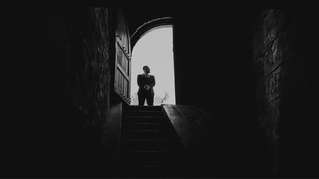 Silhouette of man in arched doorway, moody lighting.